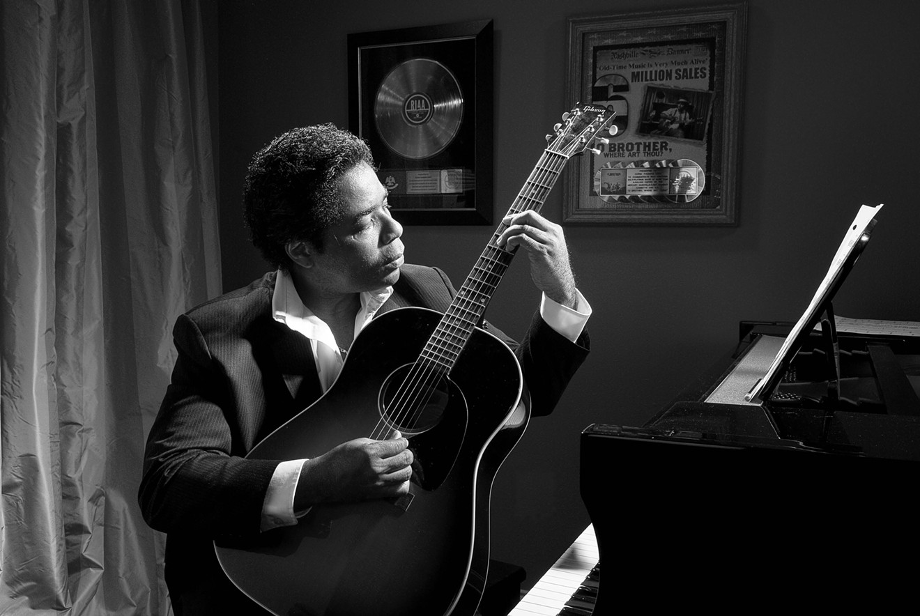 Chris Thomas King composing with guitar and piano at home. In the background are the platinum records awarded to him for being on the soundtrack of the film "O Brother, Where Art Thou?"