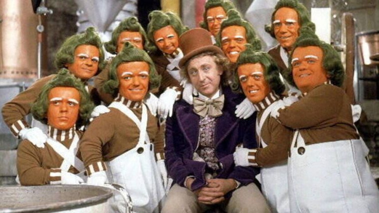 Millionaire industrialist Willy Wonka (Gene Wilder) surrounded by his immigrant, enslaved workforce, the Oompa Loompas.